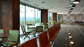 Ein modernes Restaurant mit einer langen Theke, grünen Stühlen und großen Fenstern mit Blick ins Freie.