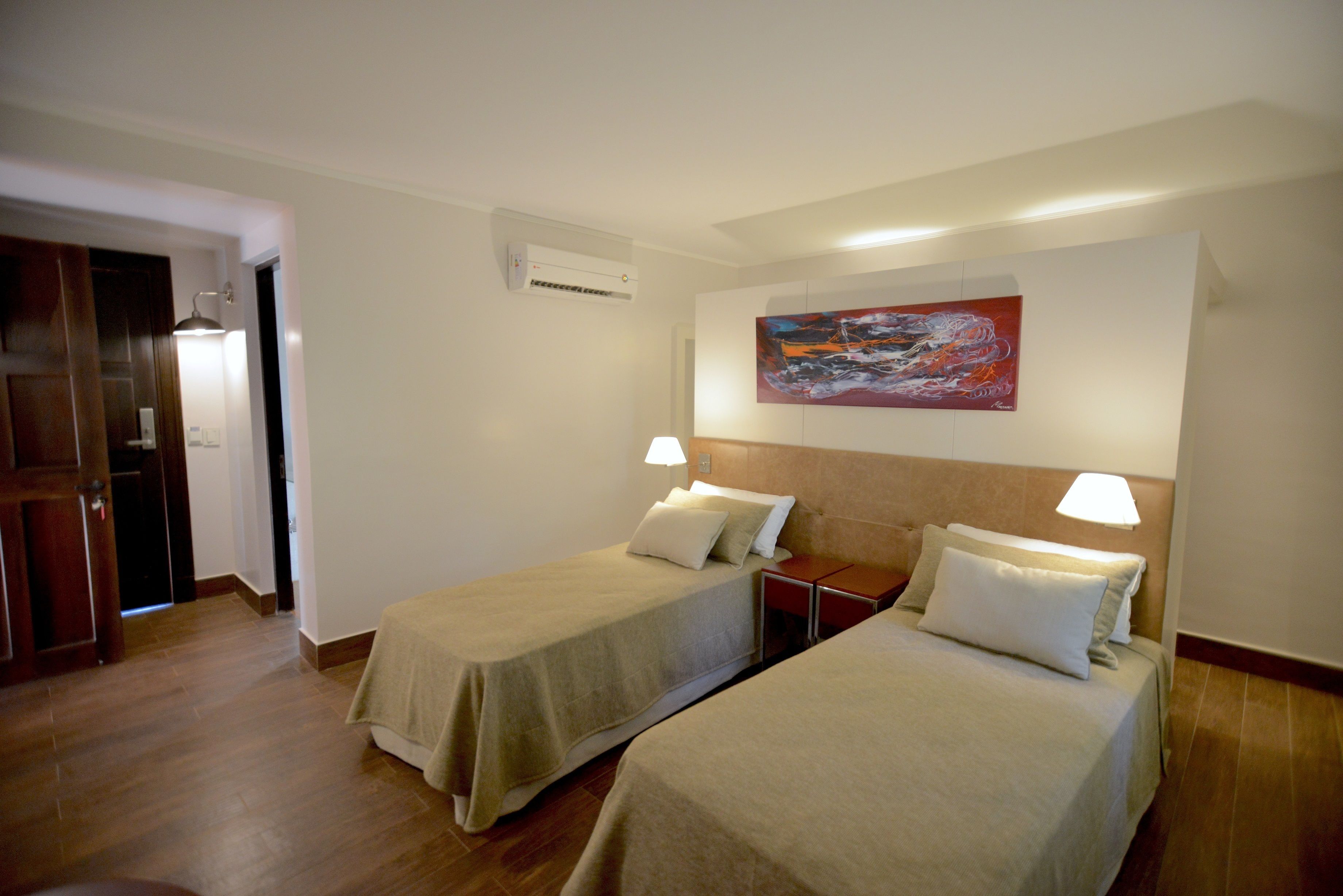 Habitación de hotel con dos camas, un cuadro en la pared, un equipo de aire acondicionado y suelo de madera.