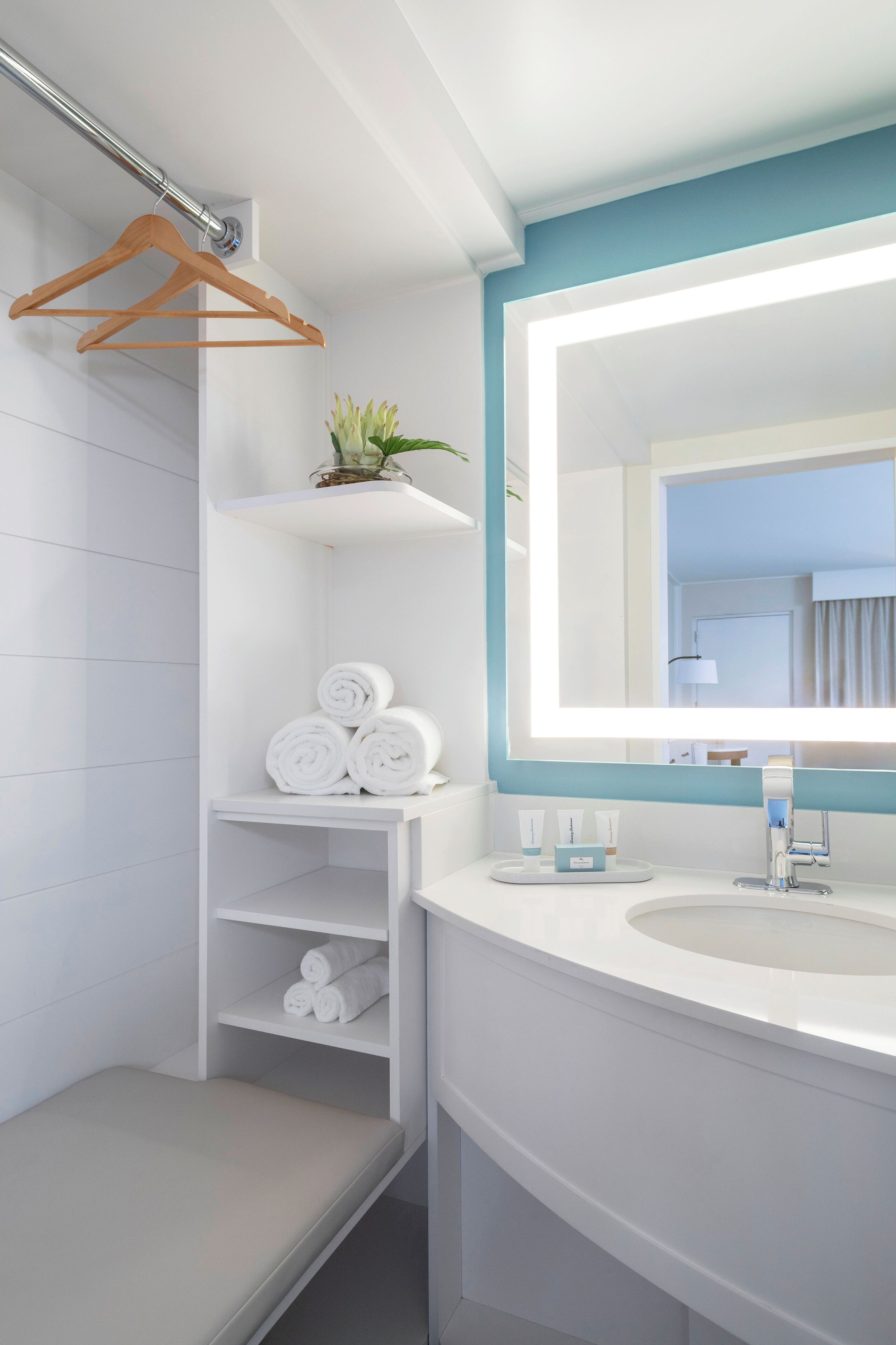 A modern bathroom with a white sink, mirror, and shelves holding towels and toiletries.