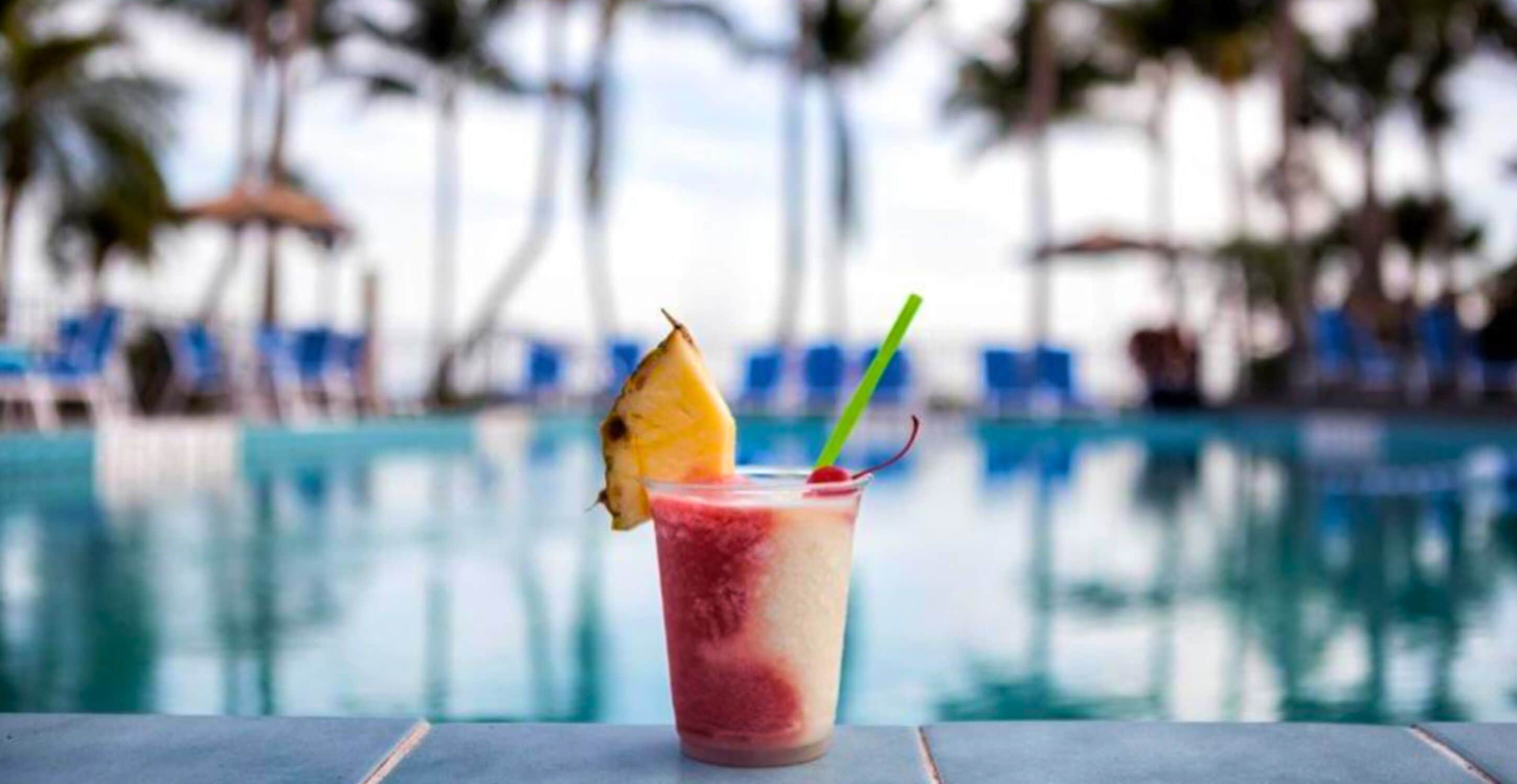 En drink med ananas og sugerør ved en pool.