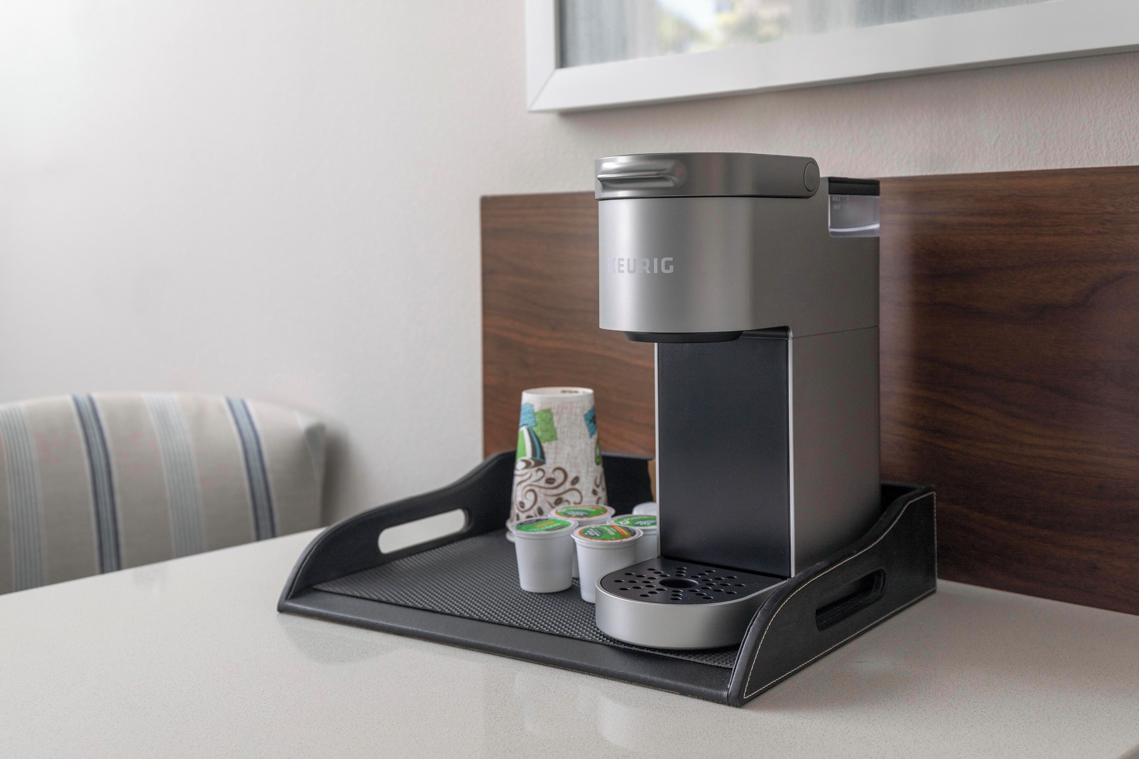 Een strak, modern koffiezetapparaat op een dienblad met wegwerpkoffiekopjes en een papieren beker, geplaatst op een tafel in een hotelkamer.