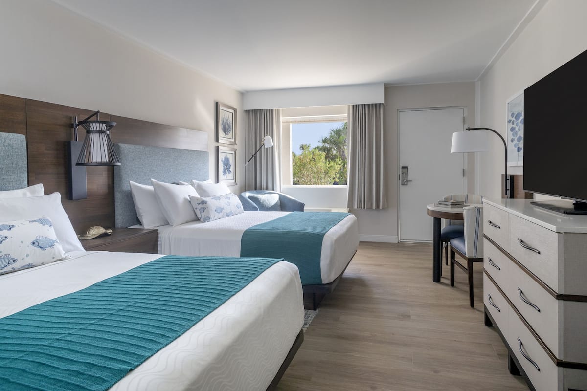 Una habitación de hotel con dos camas, un escritorio, un televisor y una ventana con cortinas.