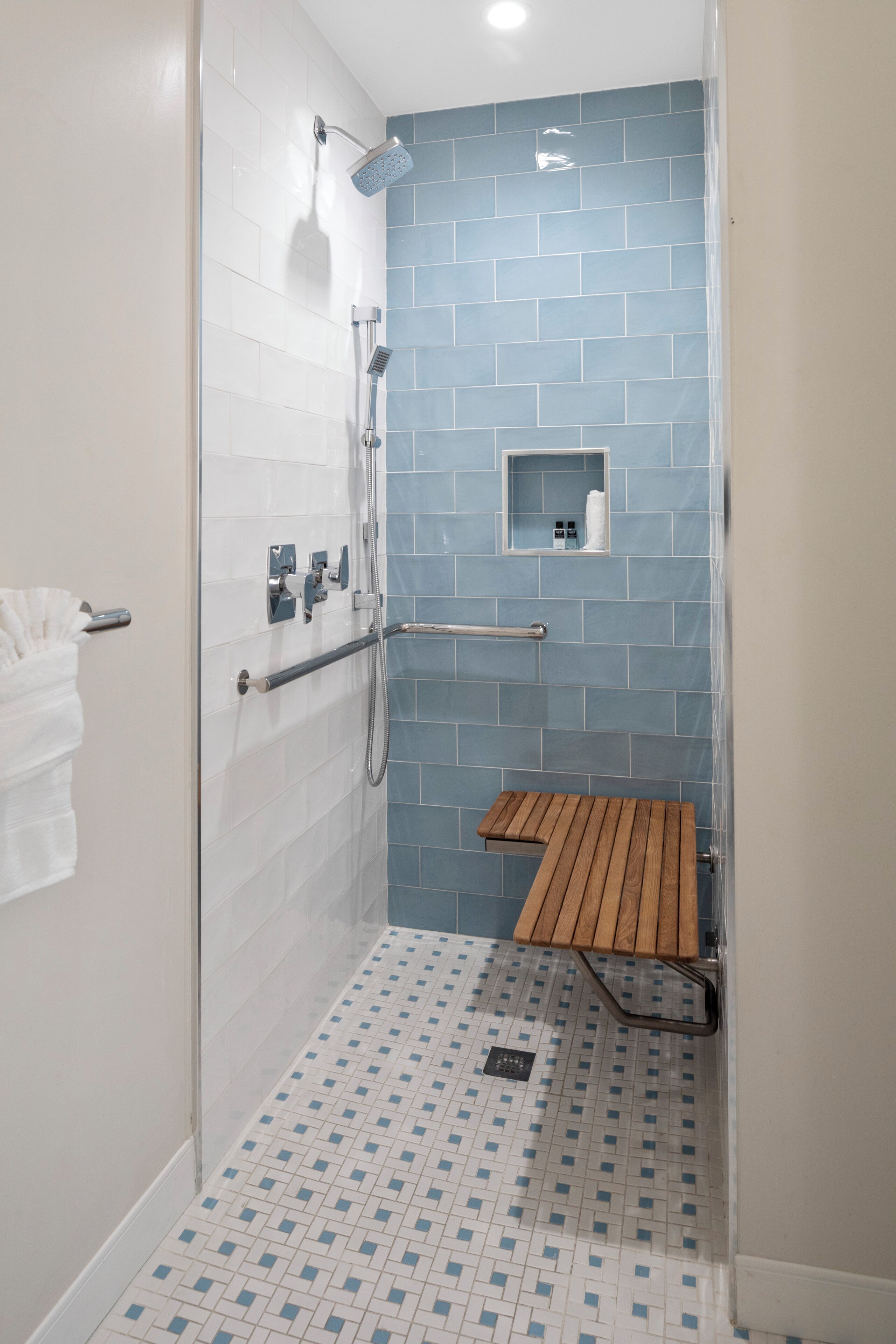 A shower area with a wooden bench, a towel rack, and a small shelf with toiletries.