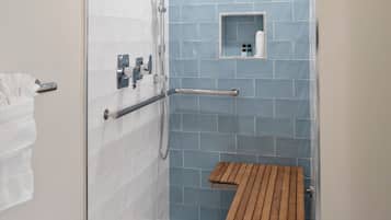 Douchegedeelte met een houten bankje, een handdoekhouder en een klein plankje met toiletartikelen.