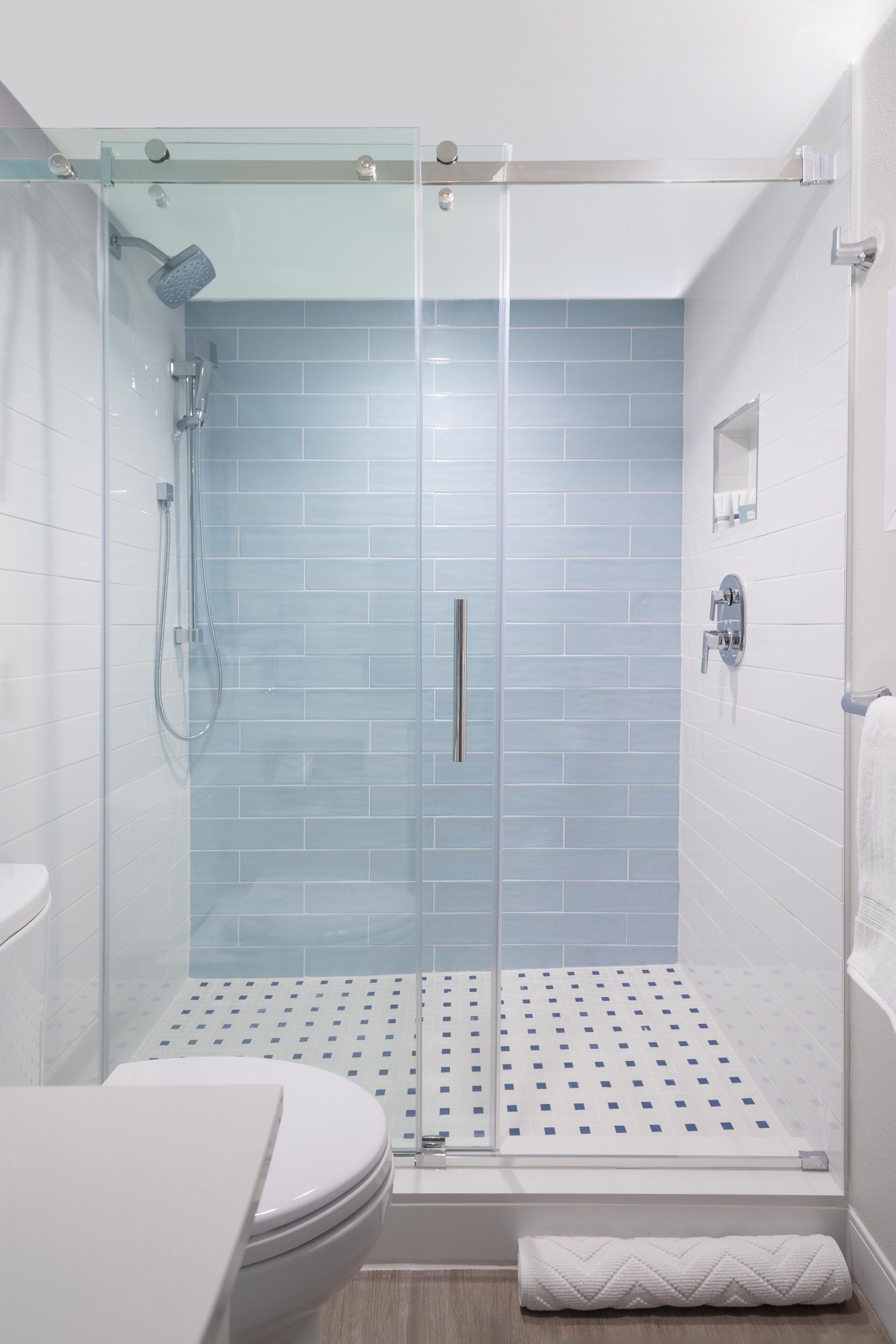 Une salle de bain moderne avec une douche à parois de verre, des carreaux blancs et un carrelage décoratif.
