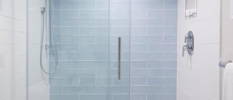 A modern bathroom with a glass-enclosed shower, white tiles, and a patterned floor.
