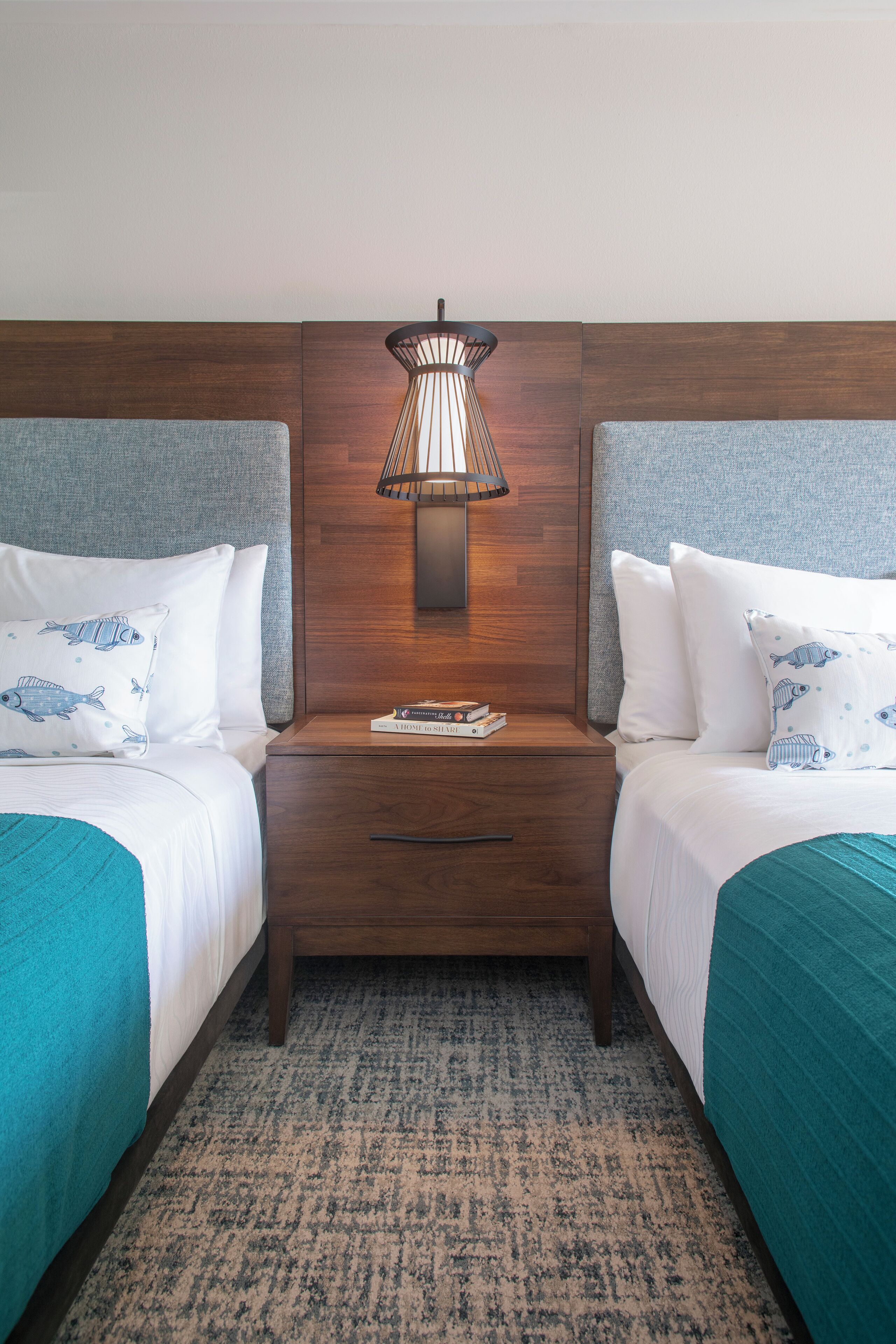 A hotel room with two beds, a nightstand with a lamp, and a textured rug.