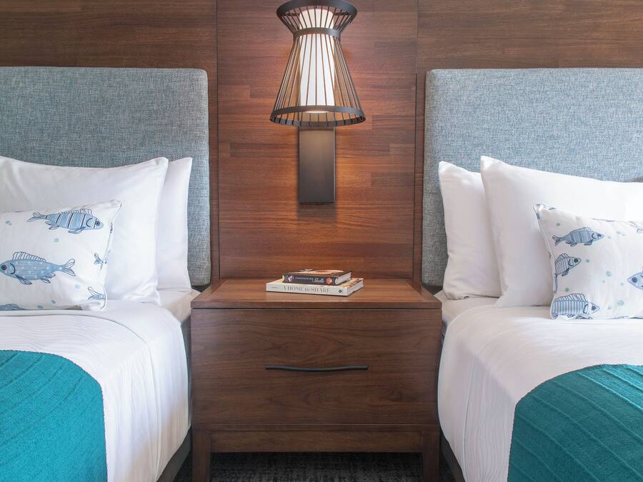 A hotel room with two beds, a nightstand with a lamp, and a textured rug.