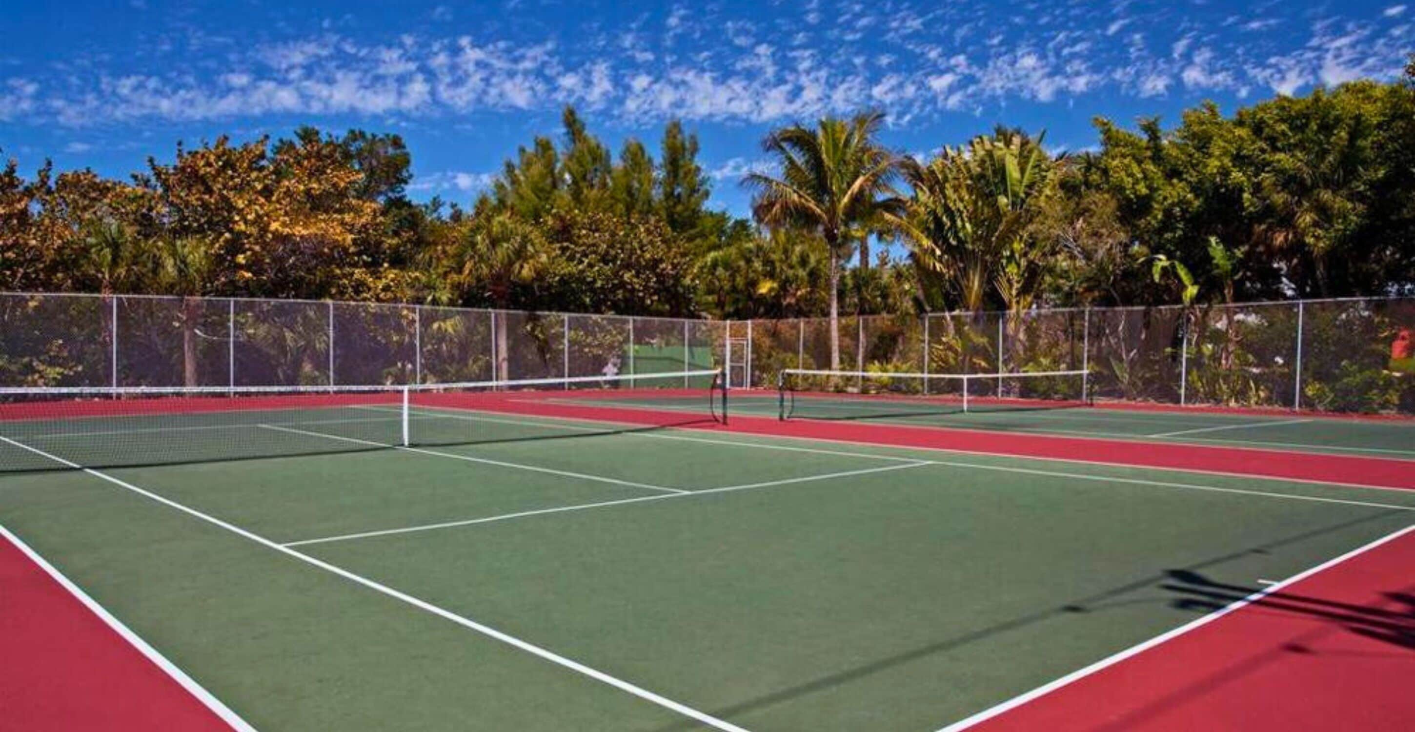 Una cancha de tenis con una red, rodeada por una cerca y árboles.