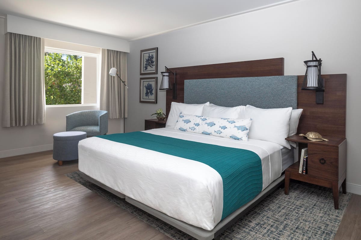 Un dormitorio con una cama grande, una mesita de noche, una silla, una ventana con cortinas y decoración en la pared.