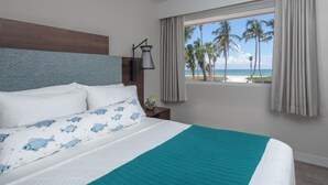 Habitación de hotel con una cama, vista a la playa y una ventana con cortinas.