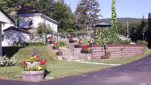 A residential area with a house, a stone retaining wall, and a garden with various plants and flowers. - Profile Motel & Cottages (Lincoln)