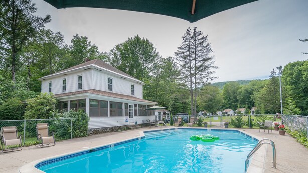 A swimming pool with a house in the background, surrounded by trees and a fence. - Profile Motel & Cottages (Lincoln)