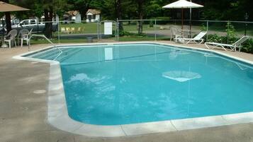 Piscina retangular com um deck de concreto, cercada por uma grade de metal. Há cadeiras de espreguiçadeira e guarda-sóis ao longo da borda da piscina.
