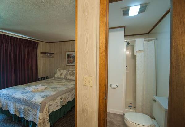 Quarto com cama, banheiro com vaso sanitário e chuveiro, e porta de madeira.