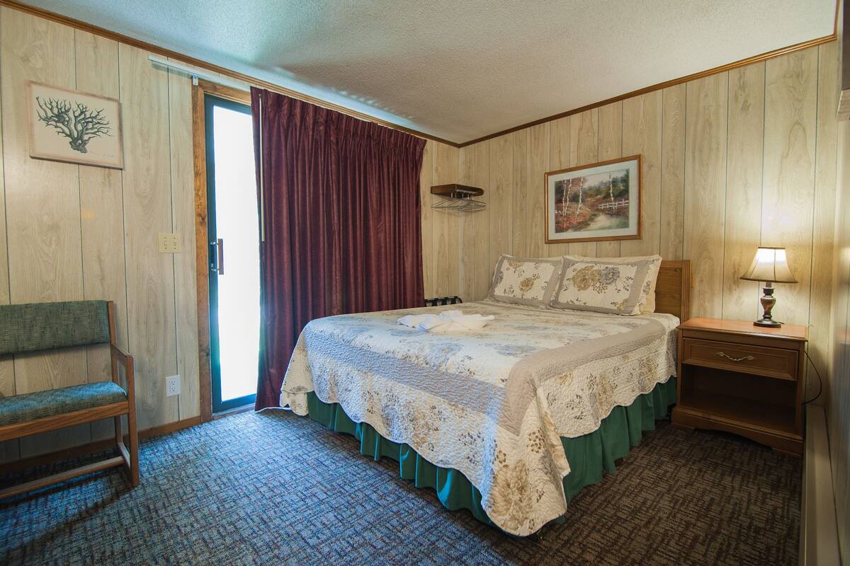 A bedroom with a large bed, a chair, a nightstand, and a door leading to a balcony.