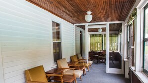 A covered porch with wooden chairs and tables, a wooden ceiling, and a view of the outdoors through open doors. - Profile Motel & Cottages (Lincoln)