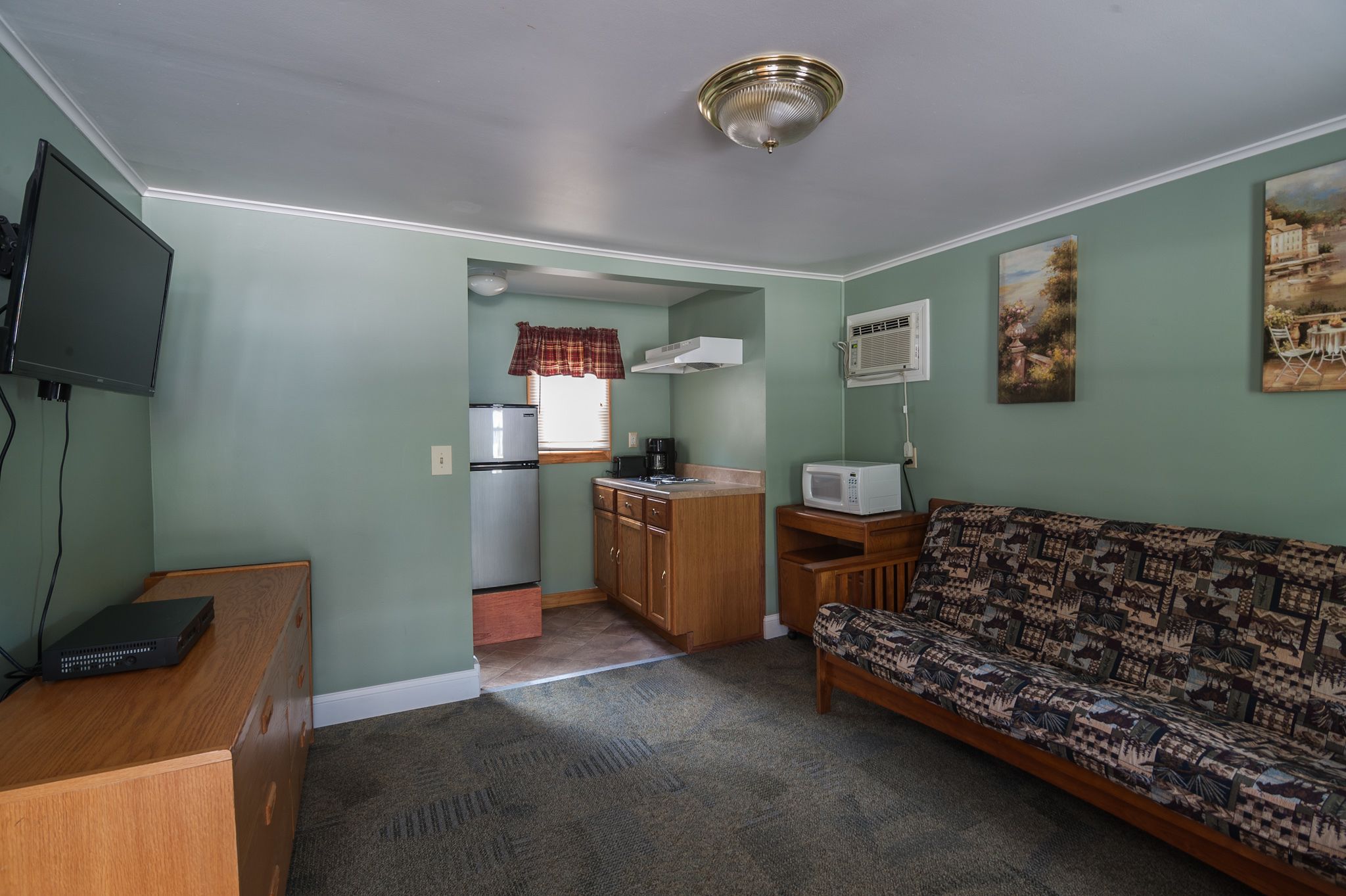 Un espacio habitable compacto con kitchenette, un sofá, un televisor y una pequeña mesa.
