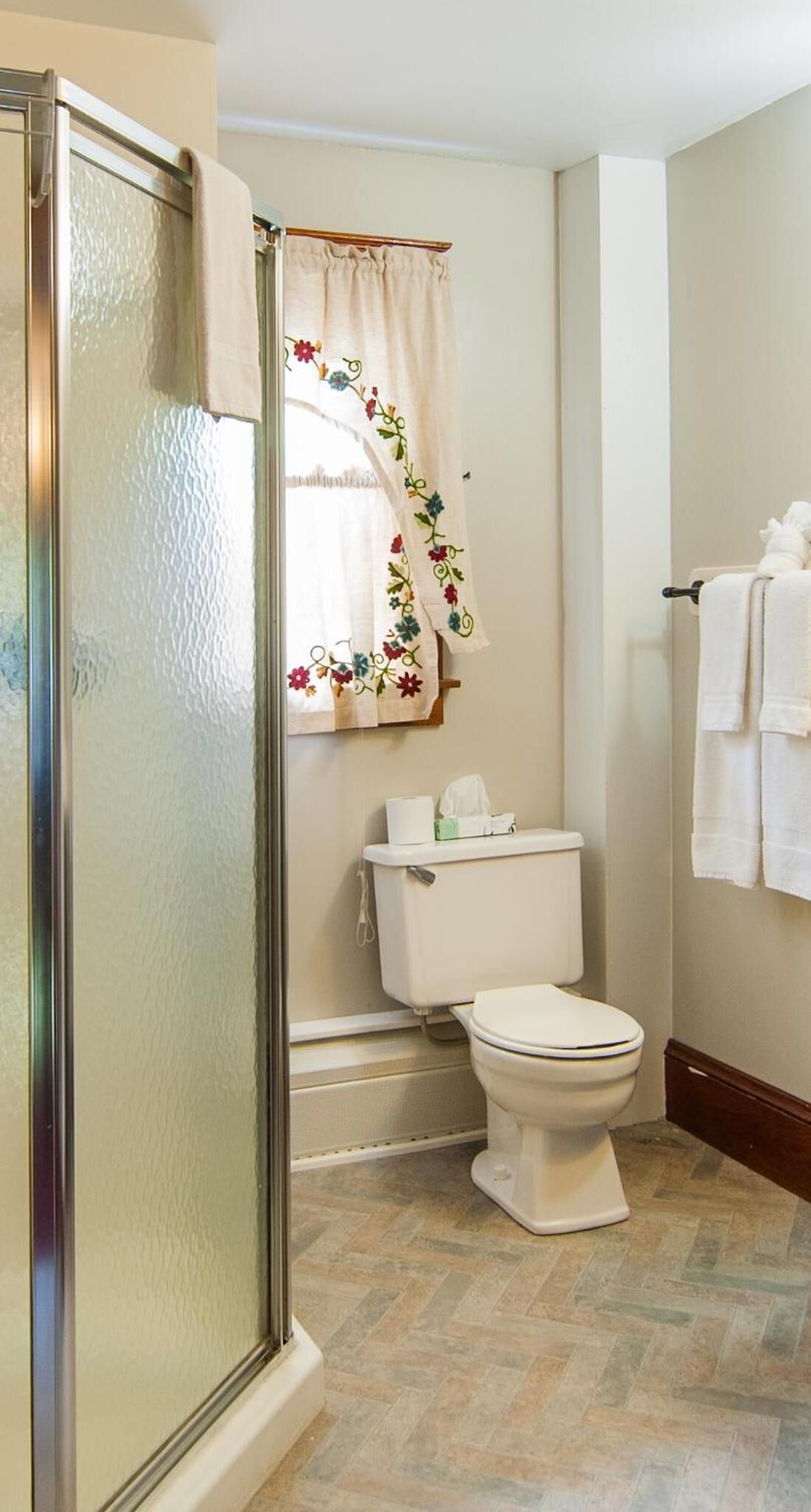 Un baño con cabina de ducha de vidrio, inodoro y ventana con cortina estampada.
