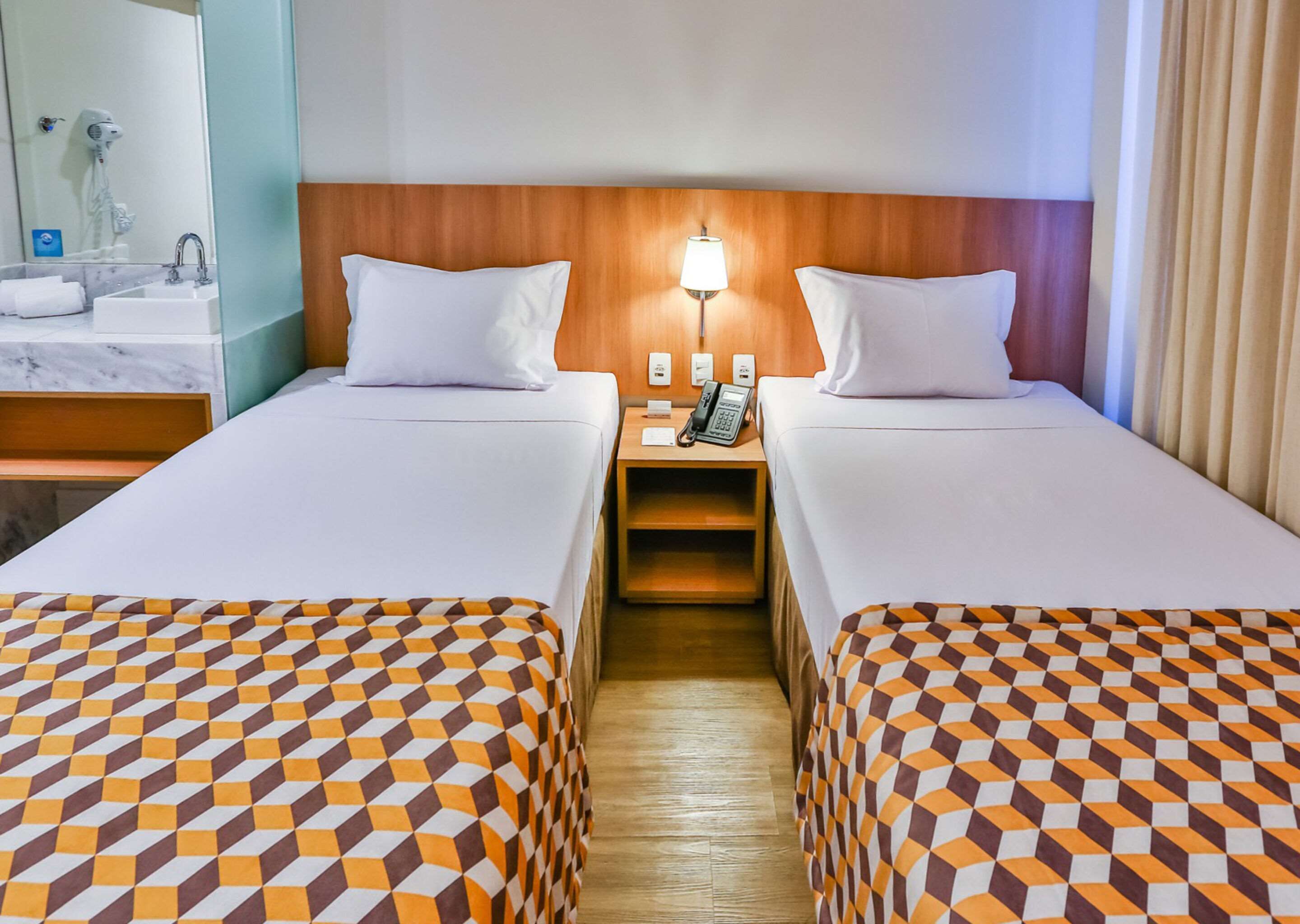 Habitació d'hotel amb dos llits individuals, un capçal de llit de fusta, una tauleta de nit amb una làmpada, un telèfon i un mirall.