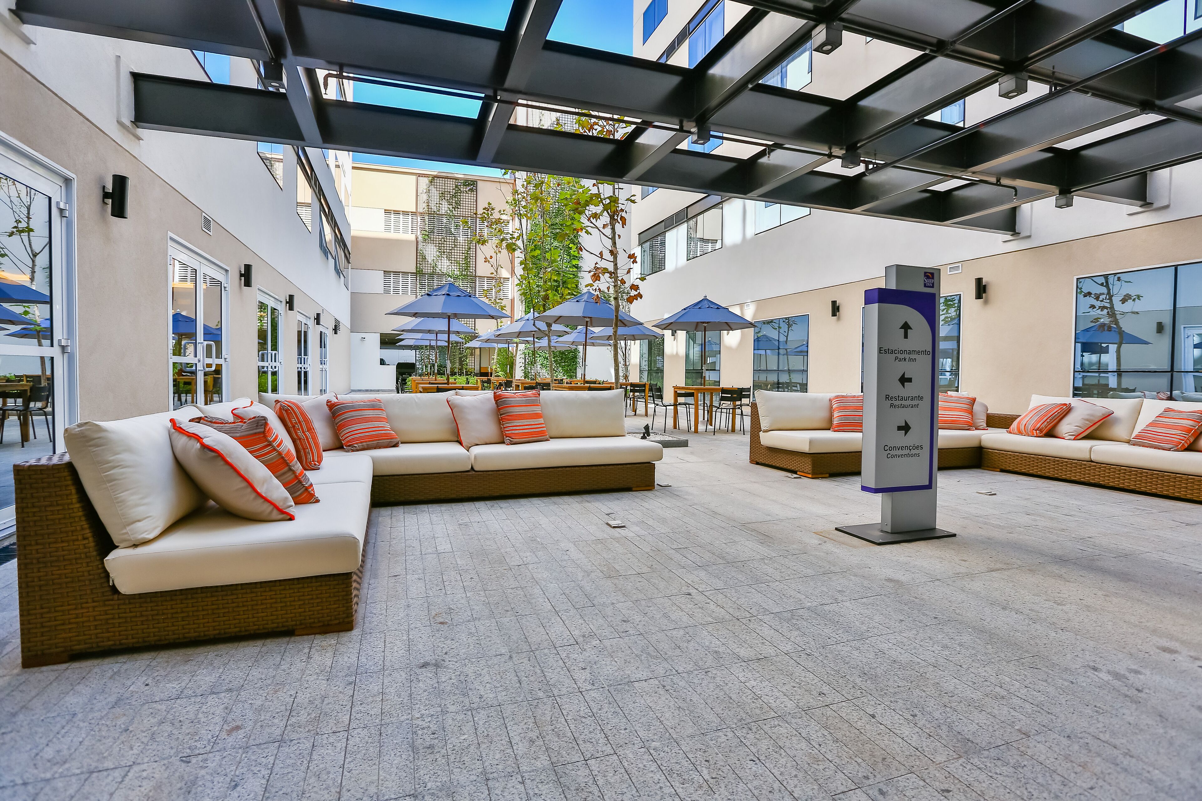 A modern outdoor seating area with sofas and umbrellas, a clear path to the restaurant, and a sign indicating the location of the restaurant and conference rooms.