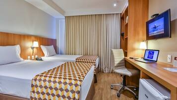 A hotel room with two beds, a desk with a computer, a TV, and a mini-fridge.