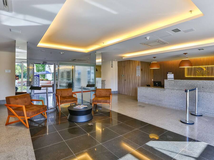 A modern hotel lobby with a reception desk, seating area, and glass doors leading outside.