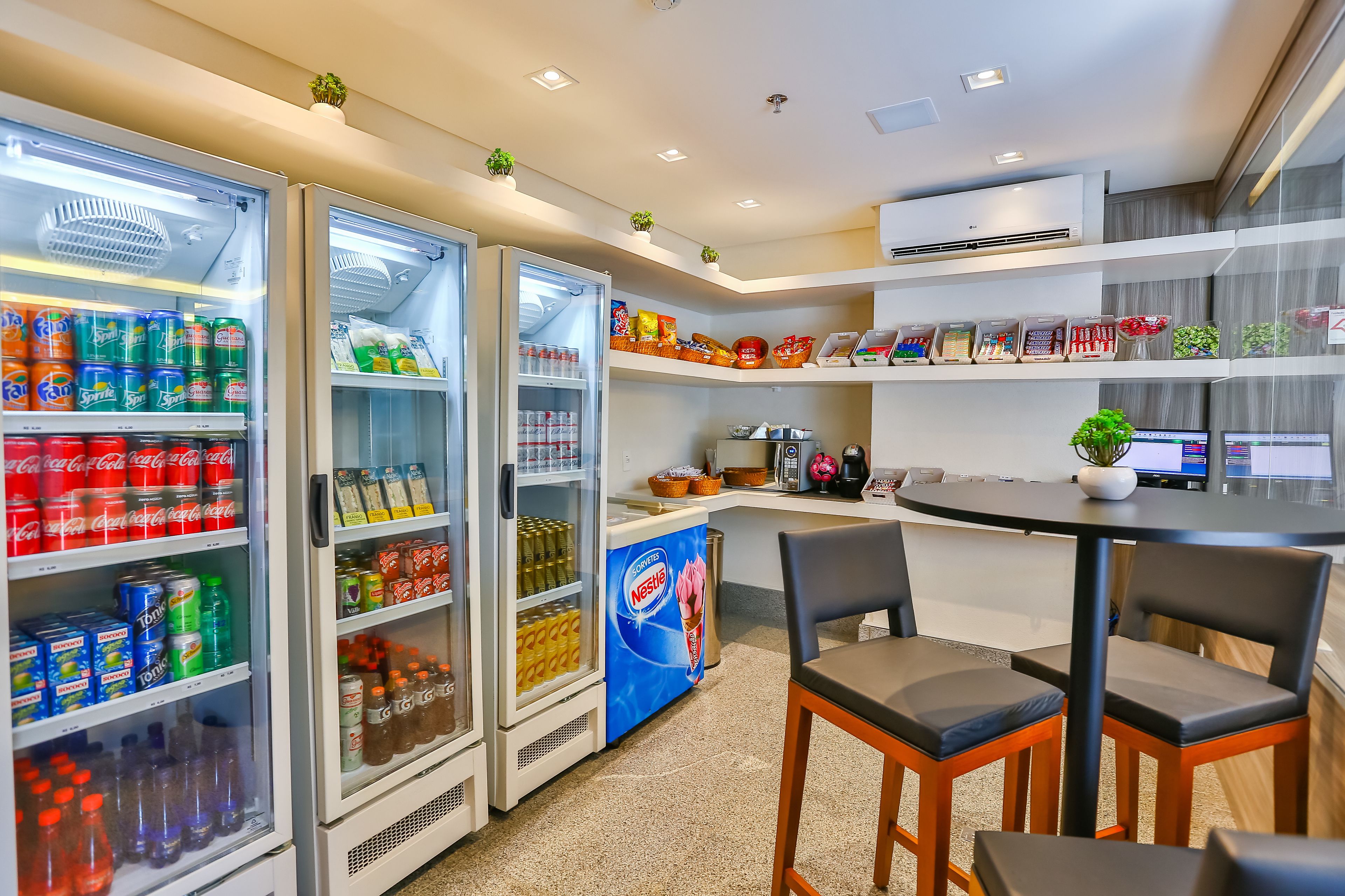 A modern kitchenette with two refrigerators stocked with beverages, a coffee machine, and a small dining area with a table and chairs.