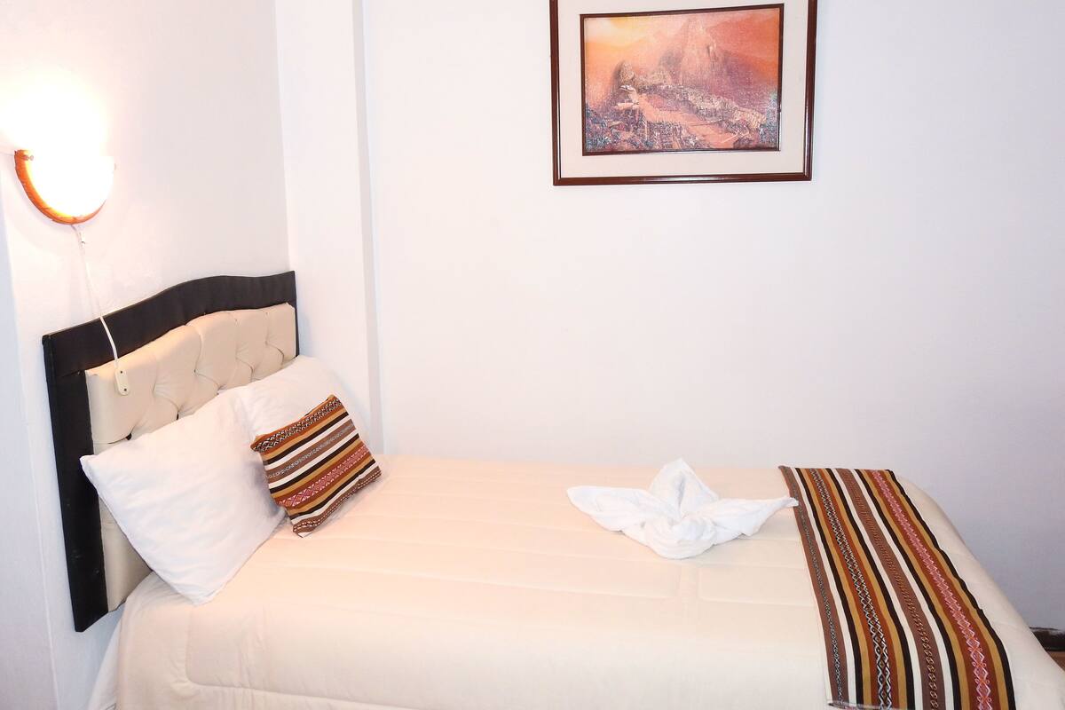 A neatly made bed with a striped blanket, a pillow, and a folded white towel.
