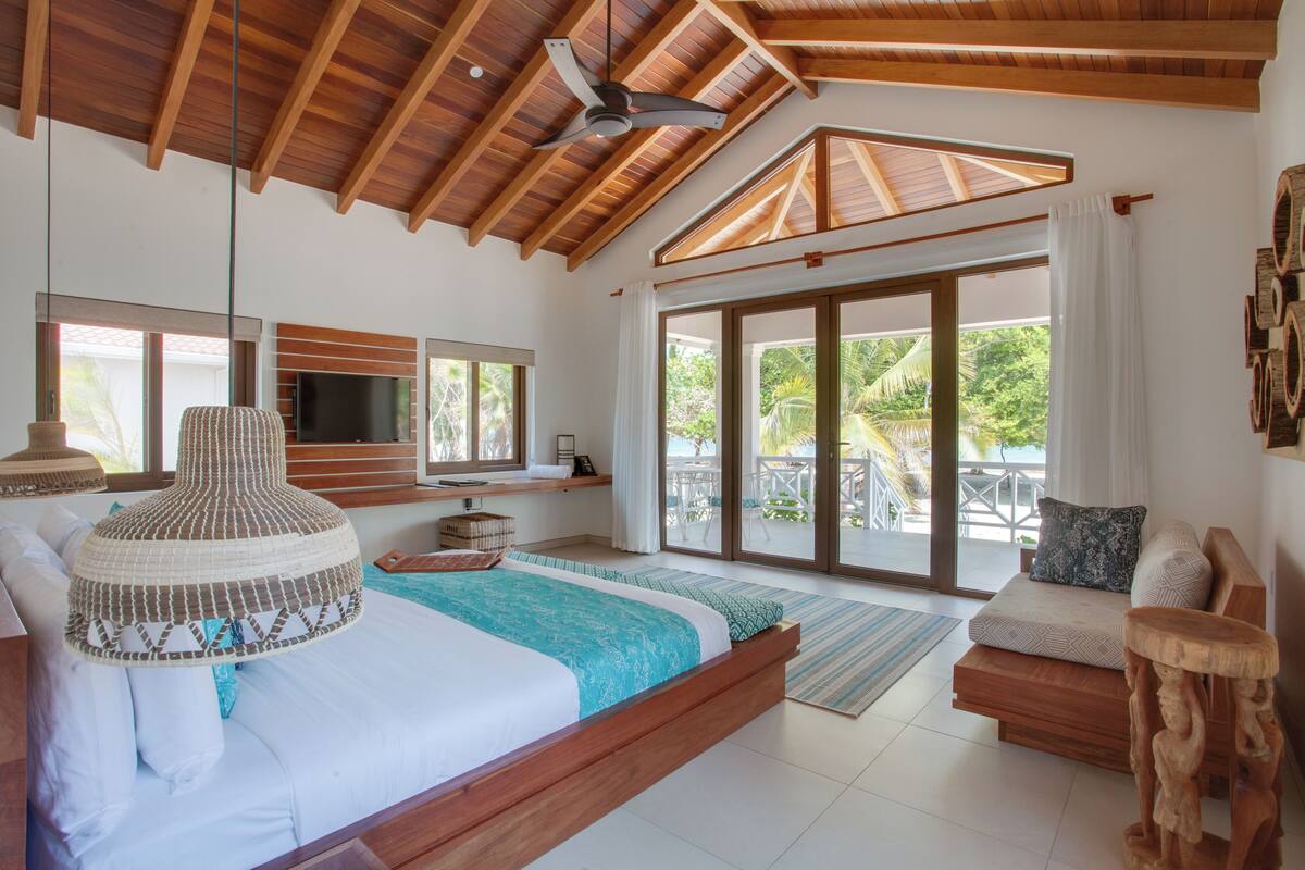 A spacious bedroom with a large bed, a ceiling fan, a TV, and a sliding glass door leading to a balcony.