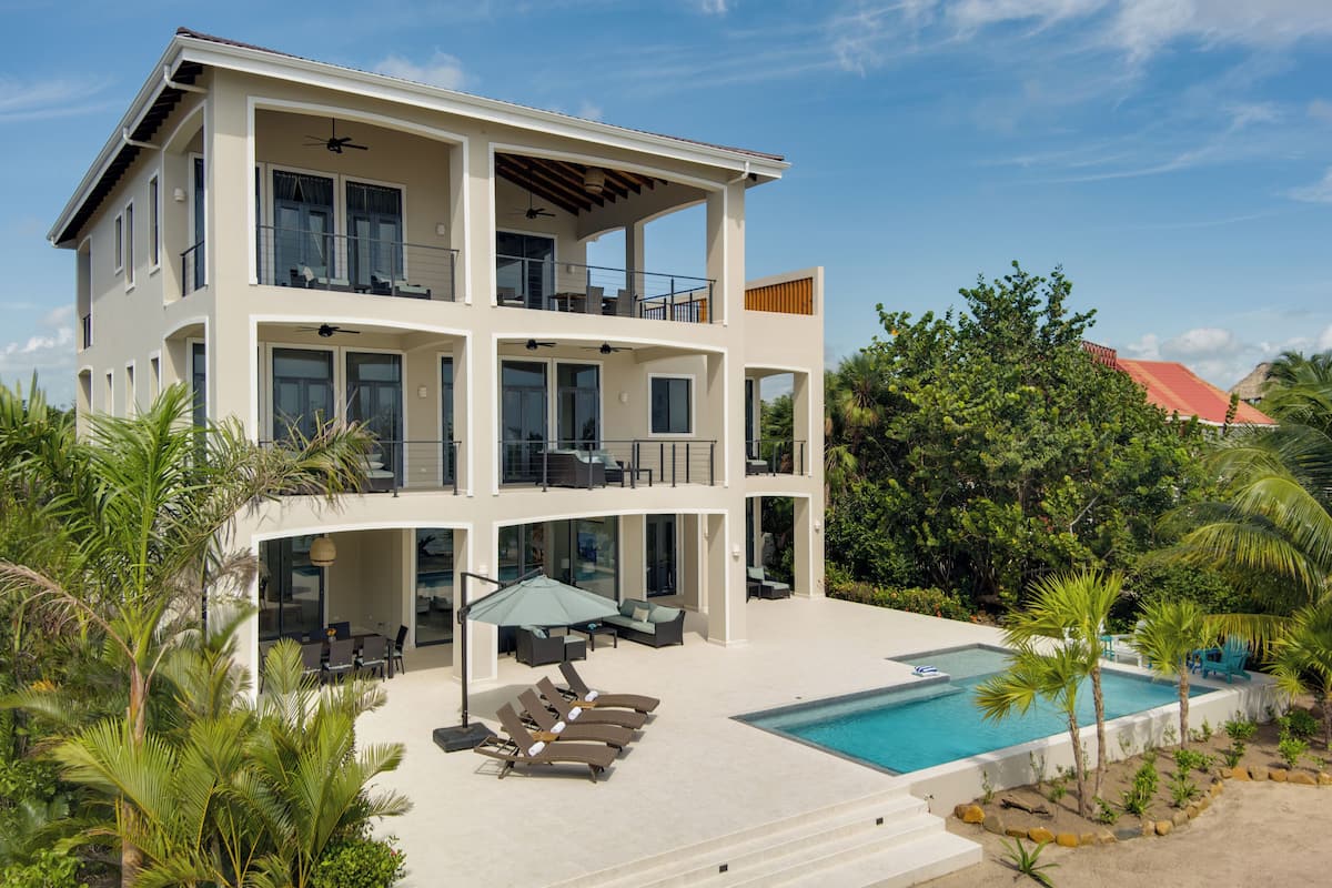 A multi-story modern house with a pool, outdoor furniture, and lush greenery.