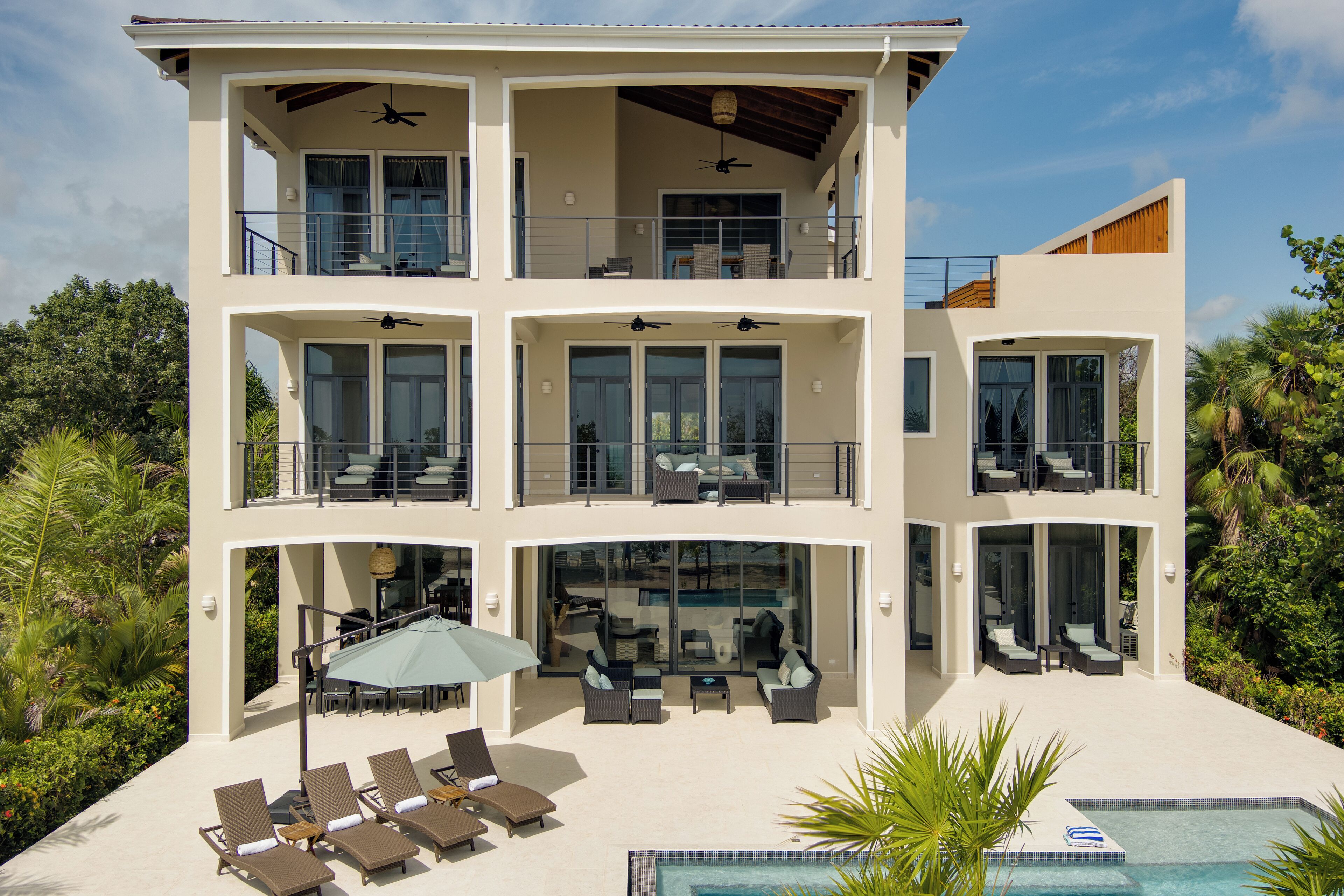 A multi-story modern house with a pool, outdoor seating, and a covered patio area.