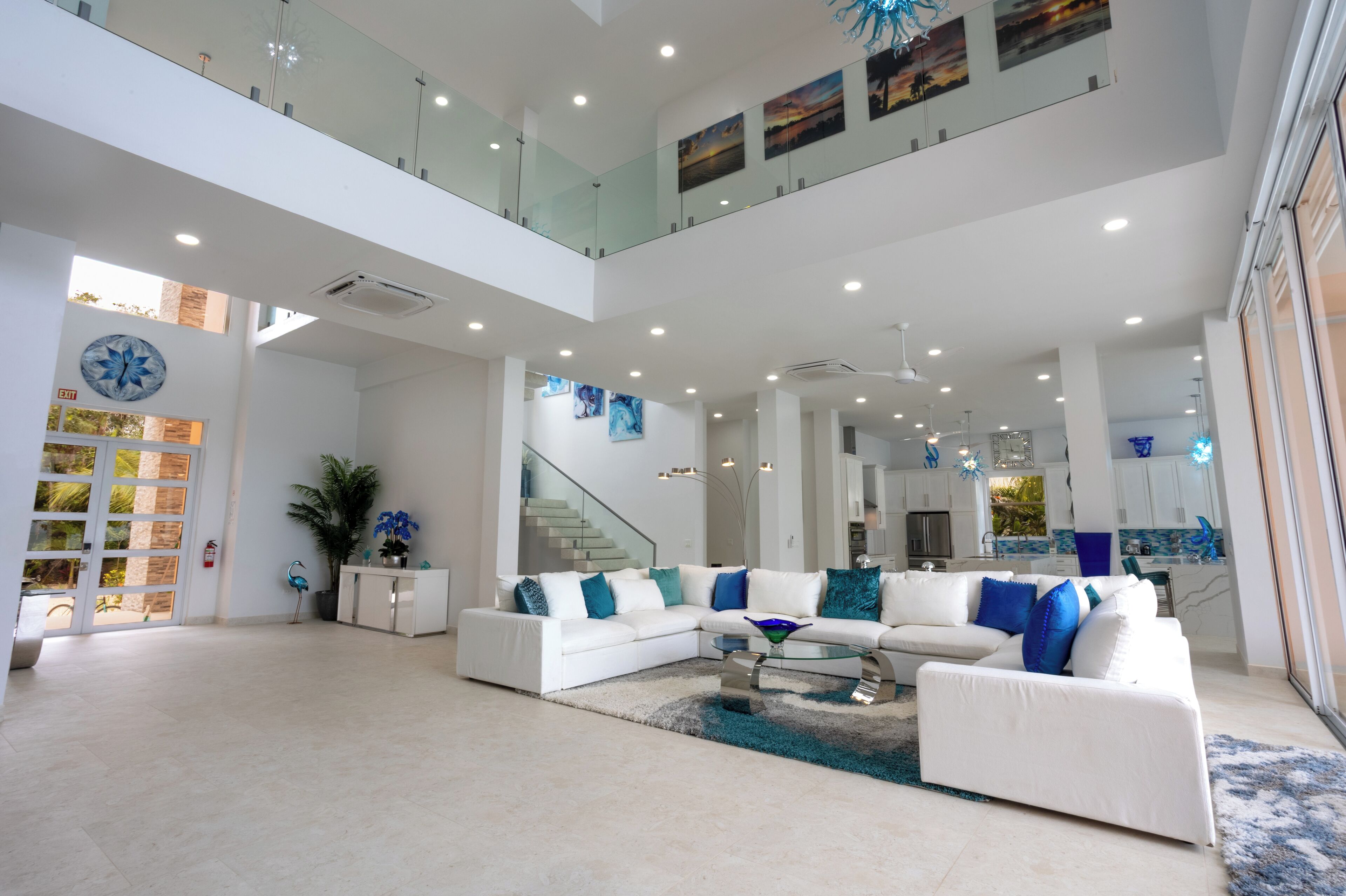 A spacious living area with a white sectional sofa, a glass coffee table, and a staircase leading to an upper level.