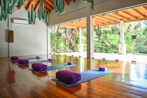 A spacious room with wooden flooring, large windows, and a view of lush greenery.