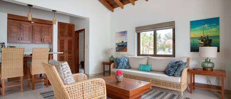 A spacious living area with wicker furniture, a wooden coffee table, and a large window with a view of the ocean.