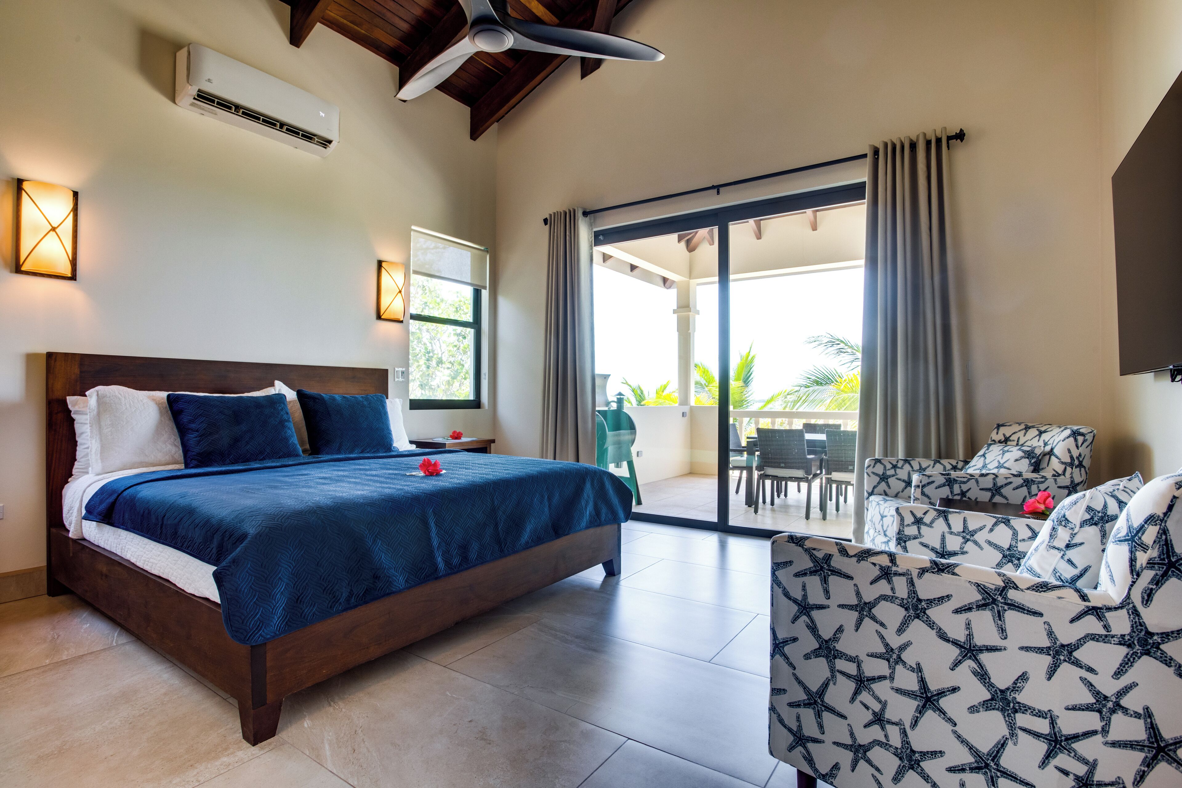 A bedroom with a bed, a sofa, a ceiling fan, an air conditioning unit, and a sliding glass door leading to an outdoor area.