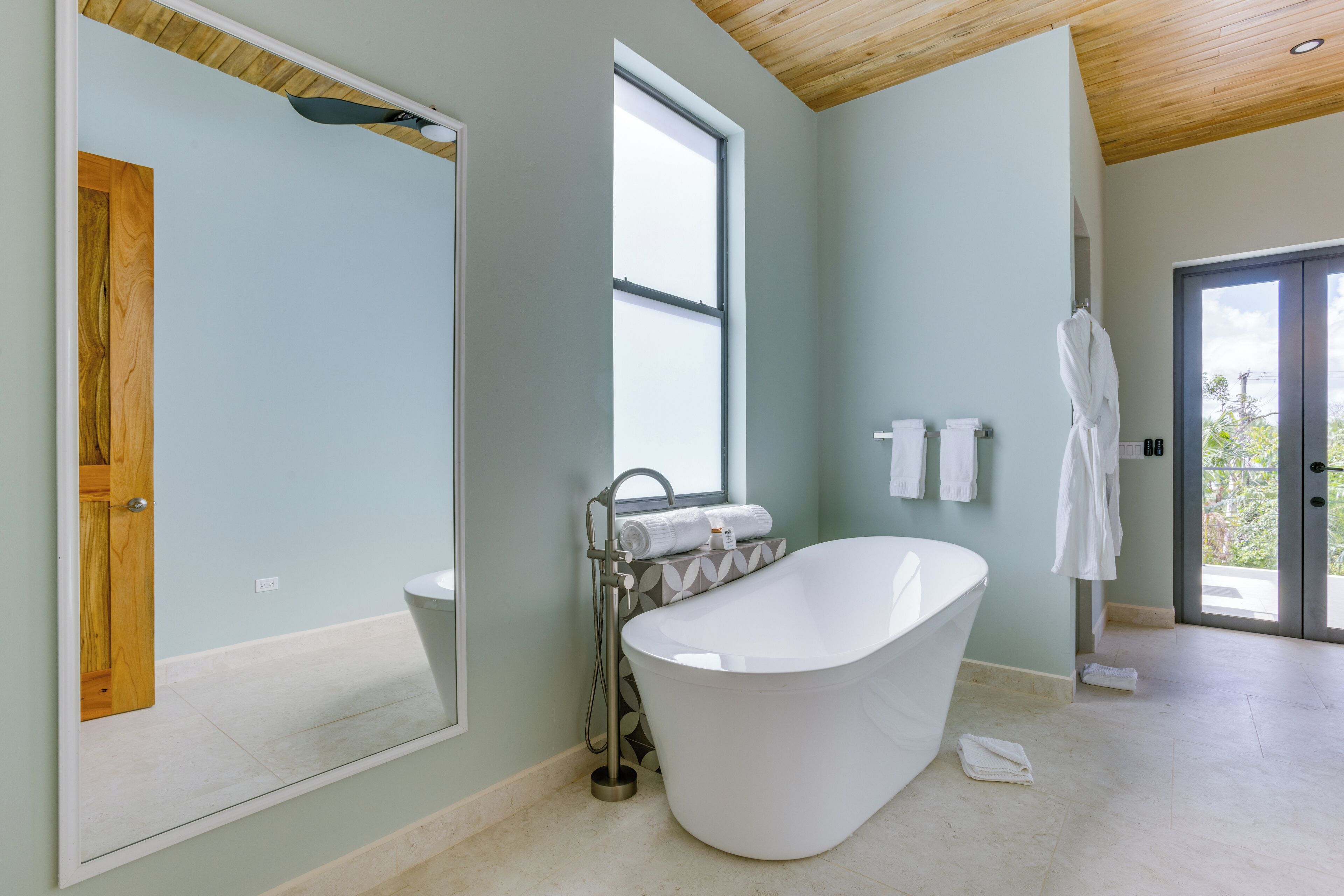 A modern bathroom with a freestanding bathtub, a large mirror, and a window providing natural light.