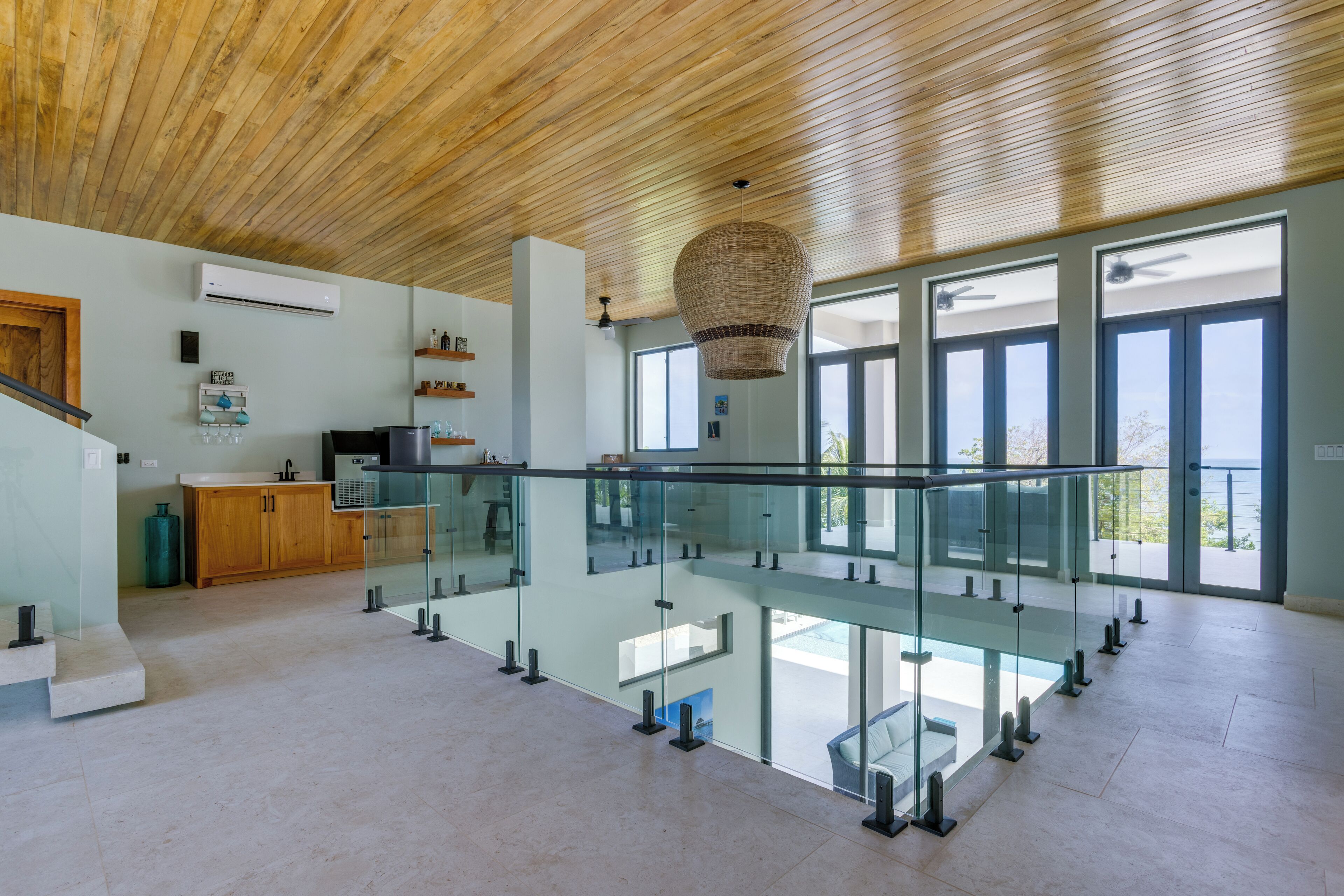 Una cocina moderna y espaciosa con techo de madera, barandilla de vidrio y vistas al exterior.