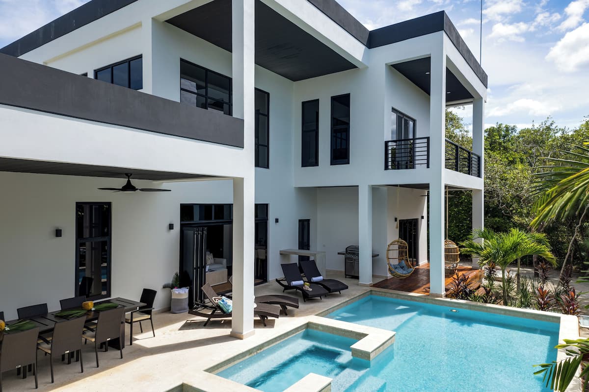 A modern two-story building with a pool, outdoor seating, and a balcony.