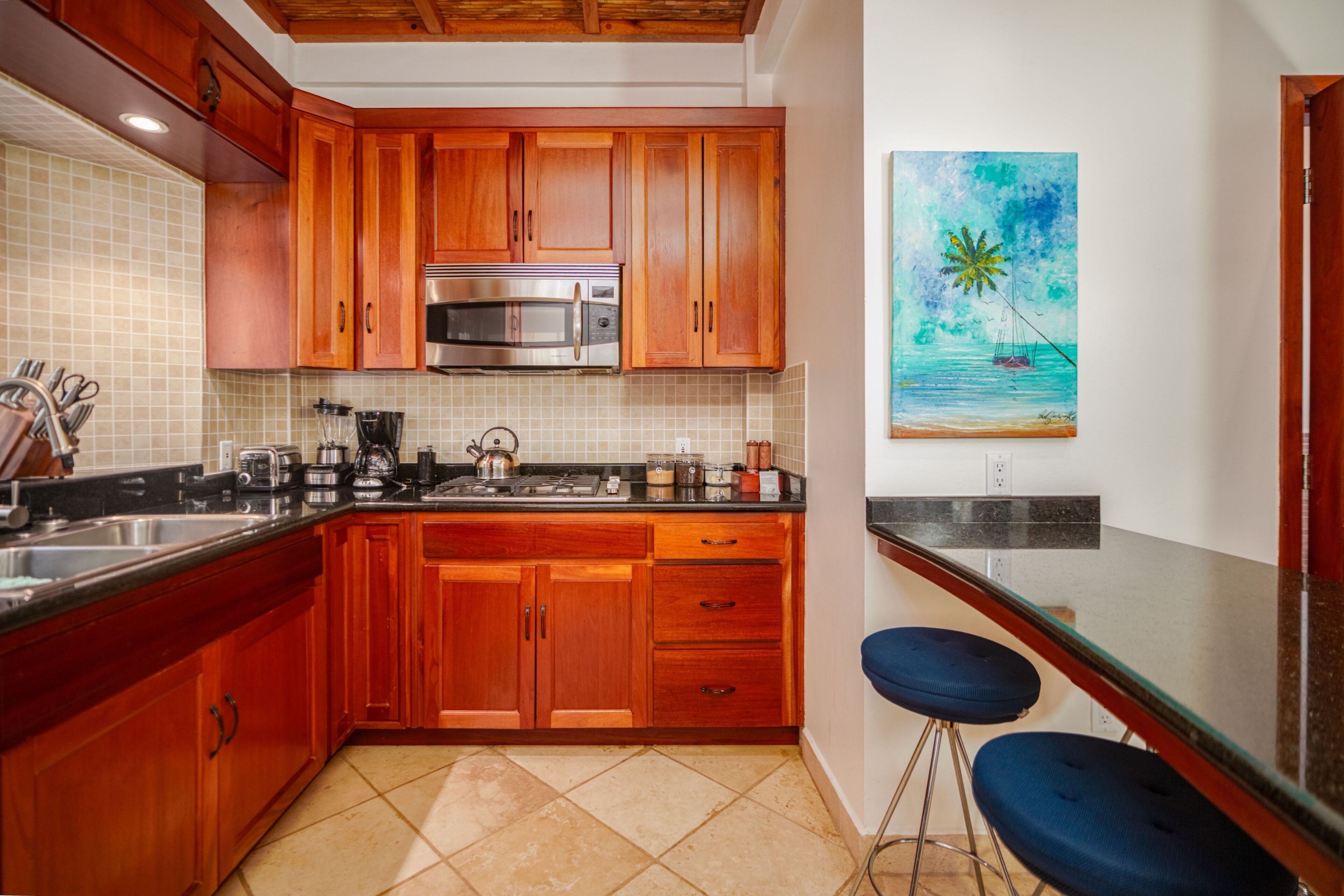 Una cocina con armarios de madera, un microondas de acero inoxidable y un cuadro de una playa.