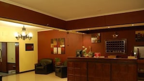 A reception area with a wooden desk, a chandelier, and a seating area with a sofa and armchairs. - Hotel Taormina (Villa Carlos Paz)