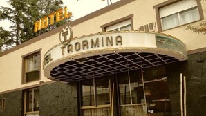 A hotel entrance with a curved awning and a sign that reads "HOTEL E. TORMINA". - Hotel Taormina (Villa Carlos Paz)