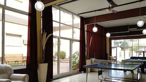 A spacious room with a ping pong table, large windows, and a comfortable chair. - Hotel Taormina (Villa Carlos Paz)