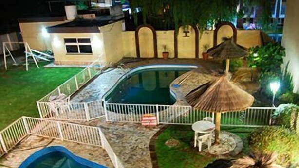 A swimming pool area with a hot tub, a small table, and a thatched umbrella. - Hotel Taormina (Villa Carlos Paz)