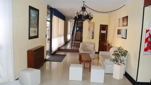 A spacious living room with a staircase, a chandelier, and a white sofa. - Hotel Taormina (Villa Carlos Paz)