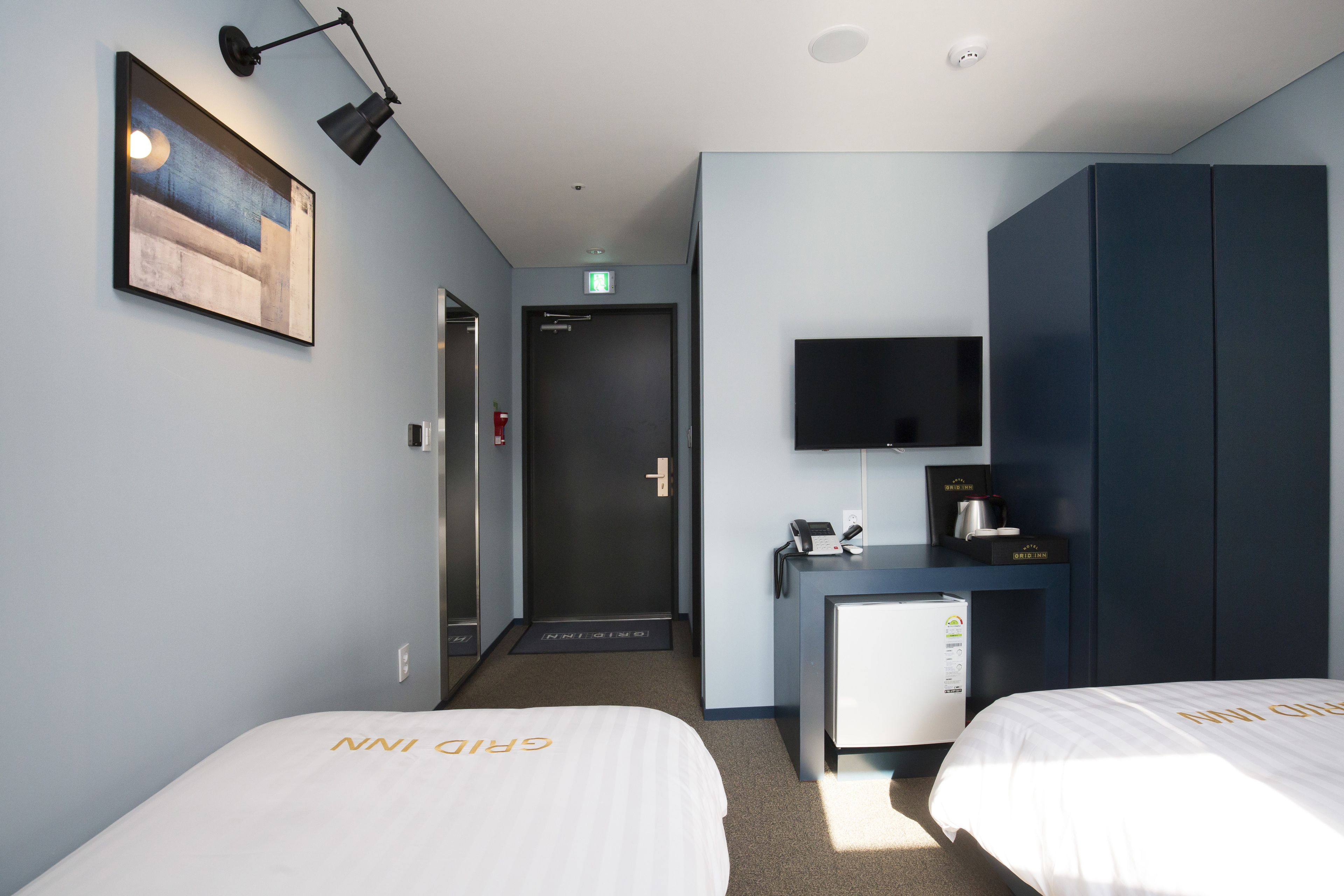 Une chambre d’hôtel avec deux lits, un bureau avec un ordinateur, une télévision et un tableau au mur.