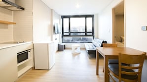A modern kitchen with white appliances, a dining area with a wooden table and chairs, and a large window offering a city view. - Grid Inn (Seoul)