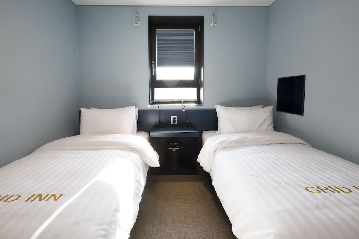 A twin room with two beds, a window, a small table, and a wall-mounted TV.