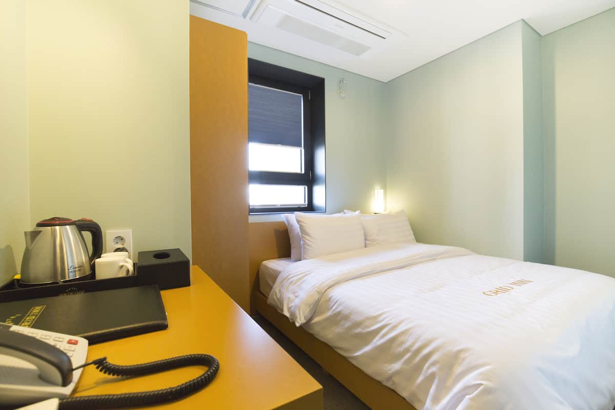 A hotel room with a bed, a desk with a telephone, a coffee maker, and a window with blinds.