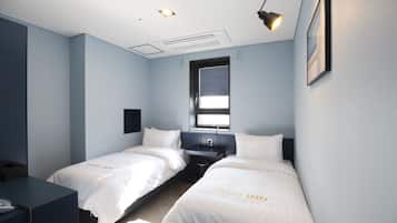 A hotel room with two beds, a desk, a window, and a ceiling light.